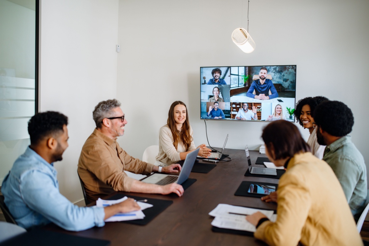 A lively and productive team meeting is captured where colleagues are connected via a large screen, showcasing a blend of in-person and remote collaboration.