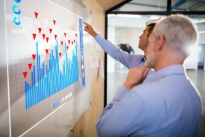 Two gentleman reviewing graphed data on a digital whiteboard.